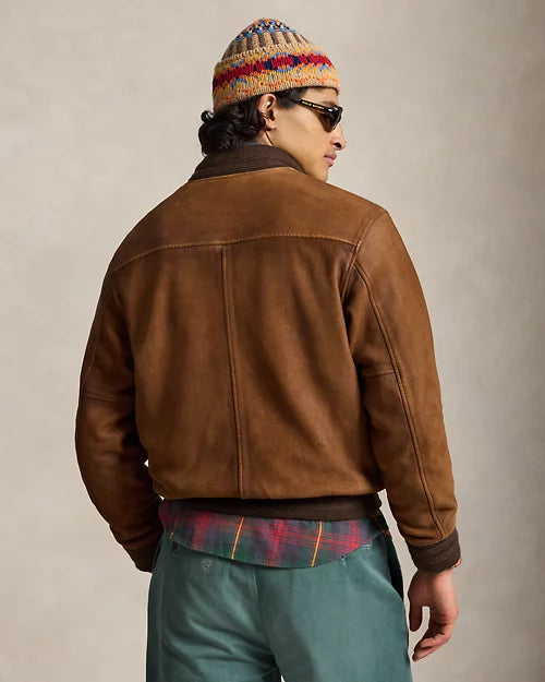 Rear model view of a brown leather varsity jacket showing the shoulder yoke, central seam, long leather sleeves and dark ribbed hem.