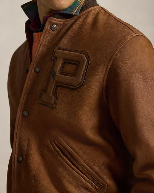 Close-up of a brown leather varsity jacket showing the raised letter P chest patch, metal snap fastenings, leather grain and welt pocket.