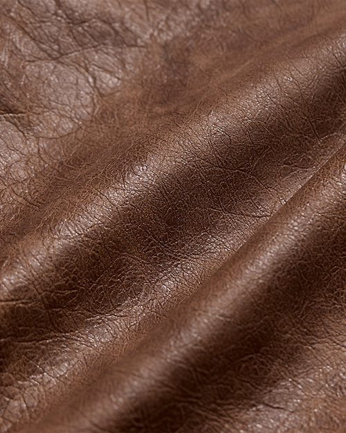 Close-up of the distressed brown leather jacket surface showing varied brown shading, fine grain, natural-looking creases and a subtle sheen.