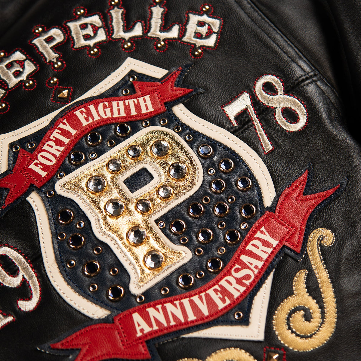 Black anniversary leather jacket shown from behind with oversized shoulder lettering, embellished artwork and a ribbed hem