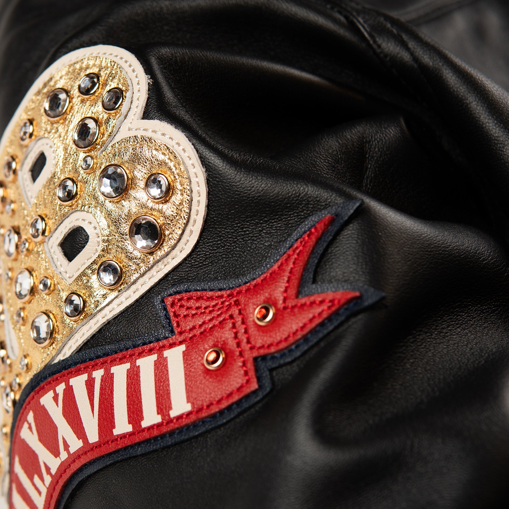 Front view of a black leather anniversary jacket with a decorated chest crest, gold-tone zipper and two angled pockets