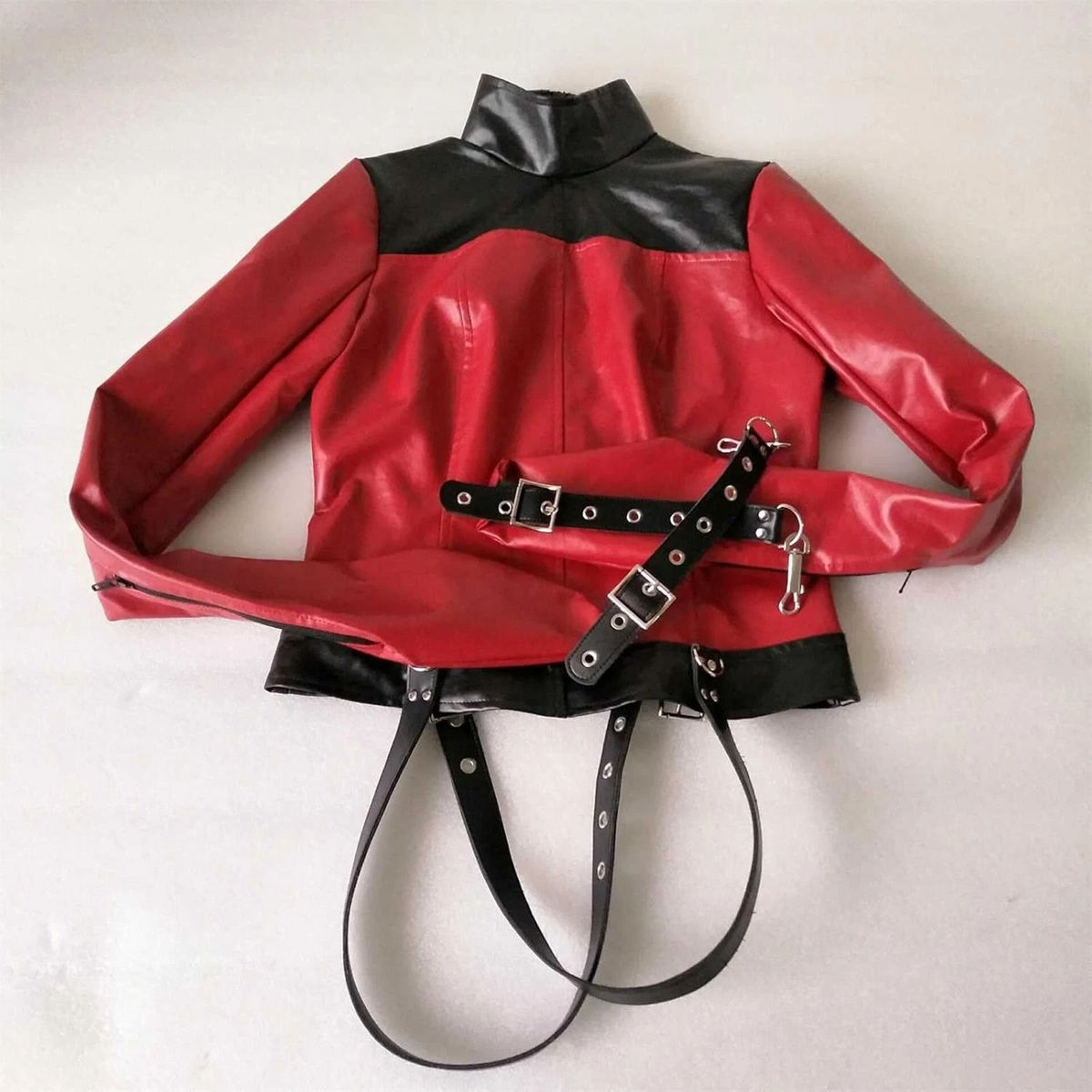 Front flat view of red leather straitjacket with black shoulder yoke and hem, standing collar, enclosed sleeves and eyeleted buckle straps.