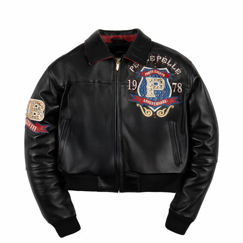Women's black leather anniversary bomber jacket, front view, with red and blue crest artwork and decorative gold-toned accents.