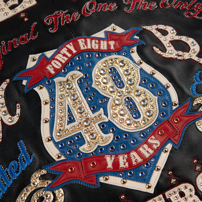 Women's black leather anniversary bomber jacket, number 48 crest close-up, with red and blue crest artwork and decorative gold-toned accents.