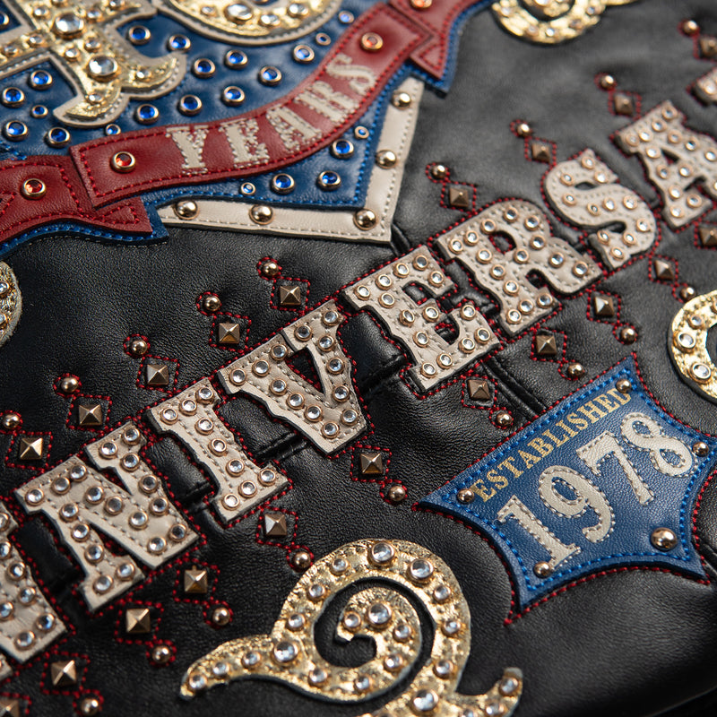 Women's black leather anniversary bomber jacket, anniversary lettering detail, with red and blue crest artwork and decorative gold-toned accents.