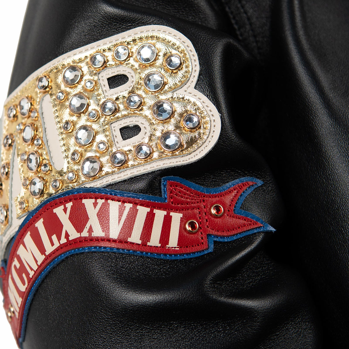 Women's black leather anniversary bomber jacket, sleeve patch detail, with red and blue crest artwork and decorative gold-toned accents.