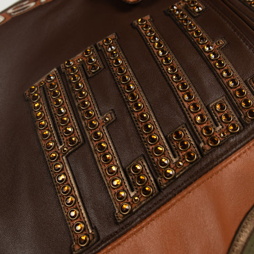 Women's brown colorblock leather racing jacket, studded lettering close-up, with caramel and olive panels and decorative metallic accents.