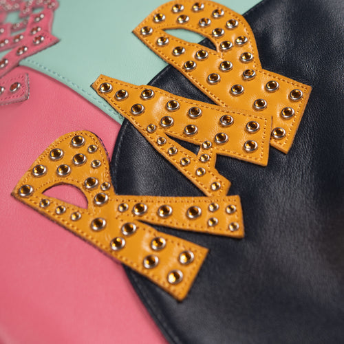 Close-up of yellow embellished lettering on the back of a multicolor leather music jacket, with pink and mint panels and visible stitching.