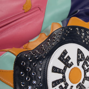 Close-up of a multicolor leather music jacket sleeve showing a studded circular emblem with yellow edging and contrasting pink leather panels.