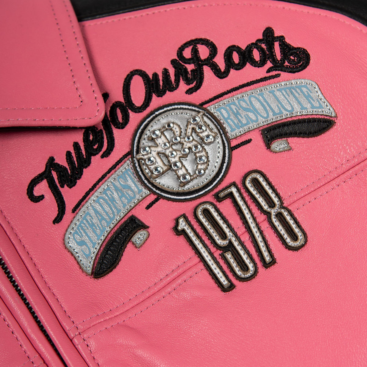 Women's pink and black leather varsity jacket, chest emblem detail, featuring contrast panels and decorative lettering in the product photo.