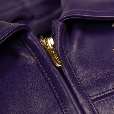 Women's purple leather bomber jacket, collar and zipper close-up, with gold-toned embellishments, cream accents, and decorative crest artwork.