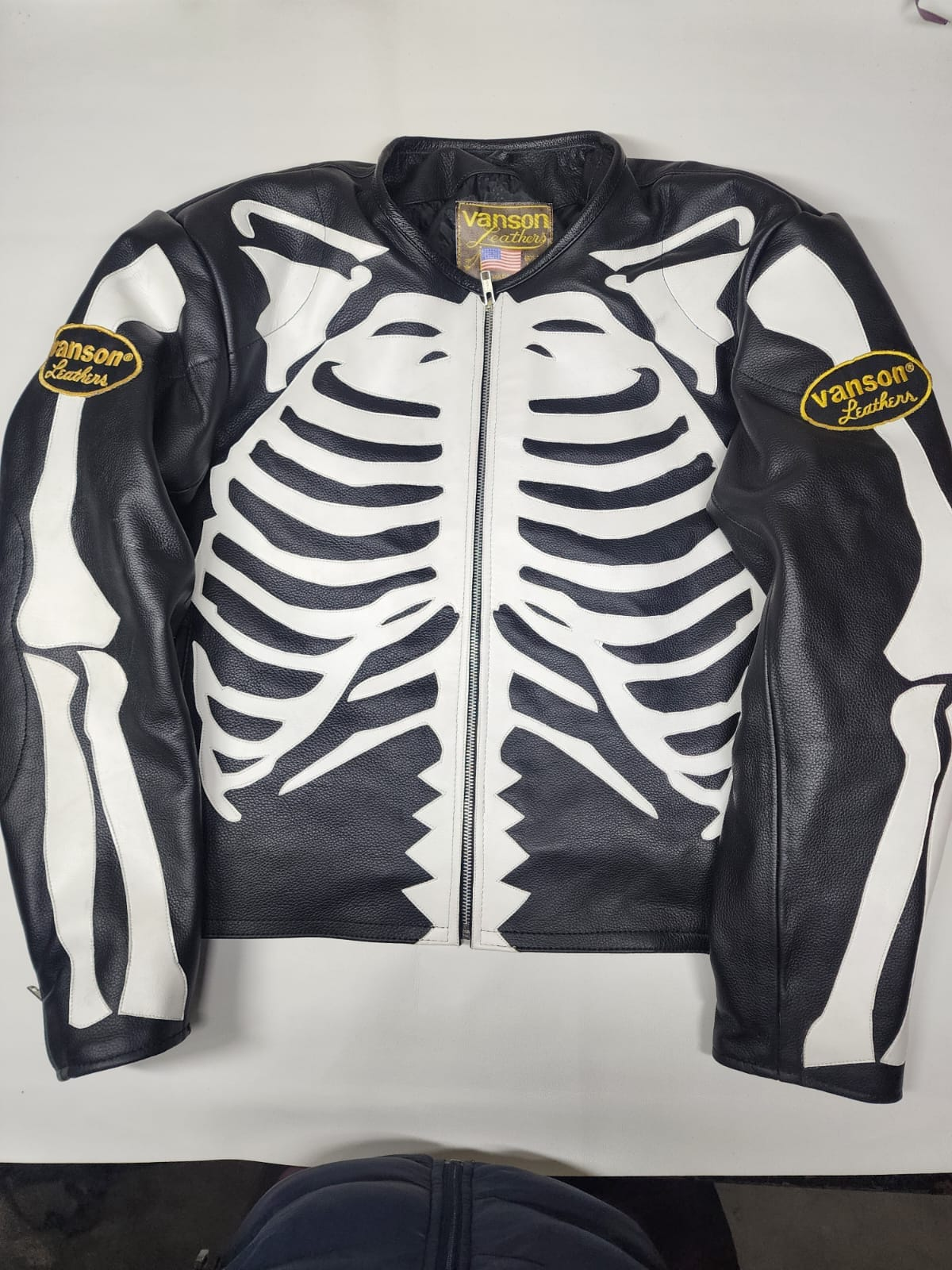 Men's black leather skeleton applique jacket, front view with contrasting white rib cage and arm bone details, center zipper and short collar.