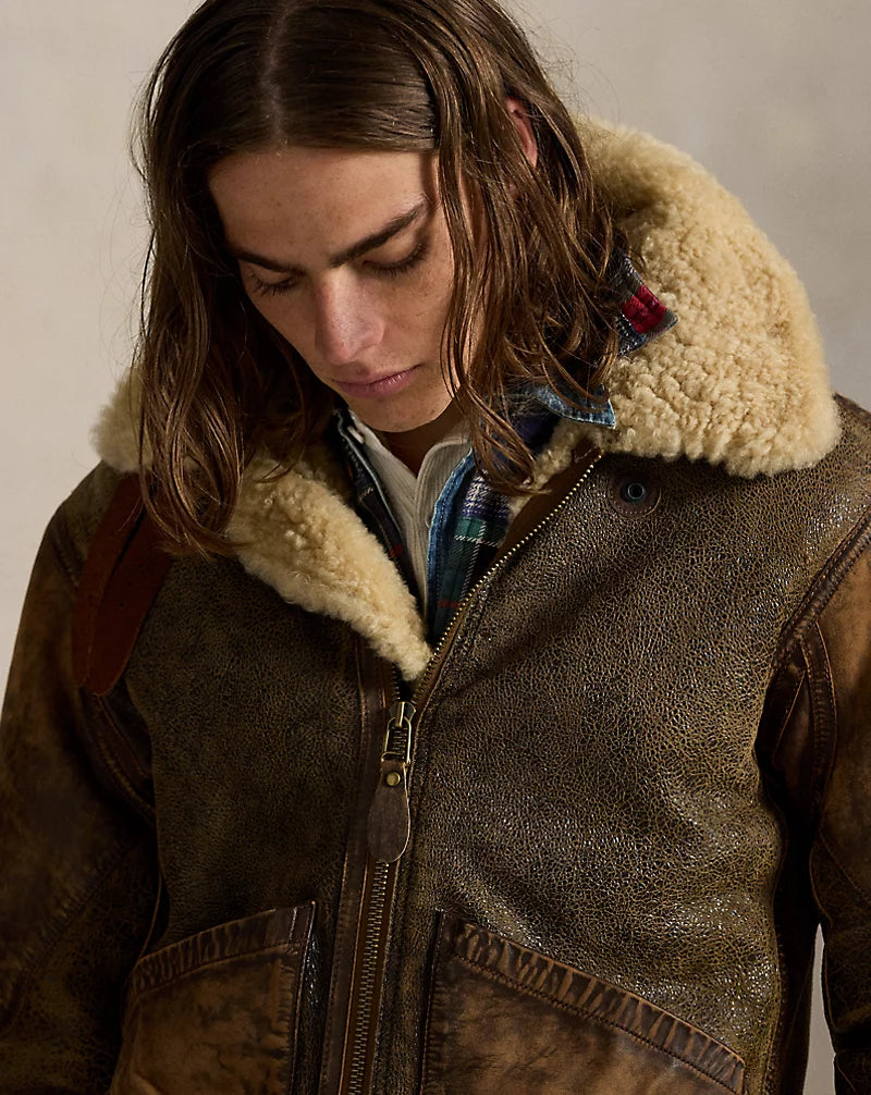 Close-up of distressed brown leather aviator jacket showing cream textured collar, front zipper, leather pull tab and pocket edges.