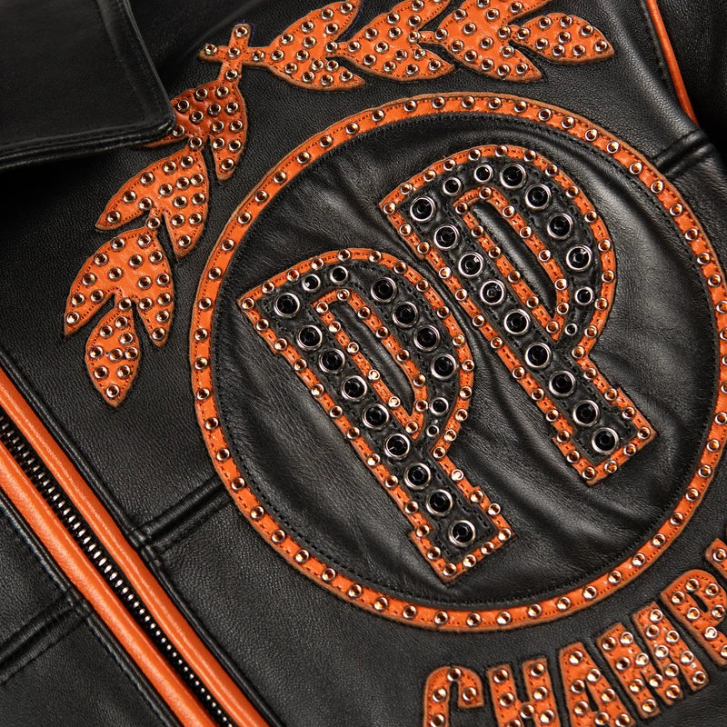 Close-up of the Pelle Pelle Champions jacket showing a black PP monogram, orange laurel appliqué and reflective metallic embellishments.