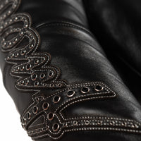 Sleeve detail of women's black leather racing jacket showing script applique, metallic stitching and rows of silver-tone eyelets.