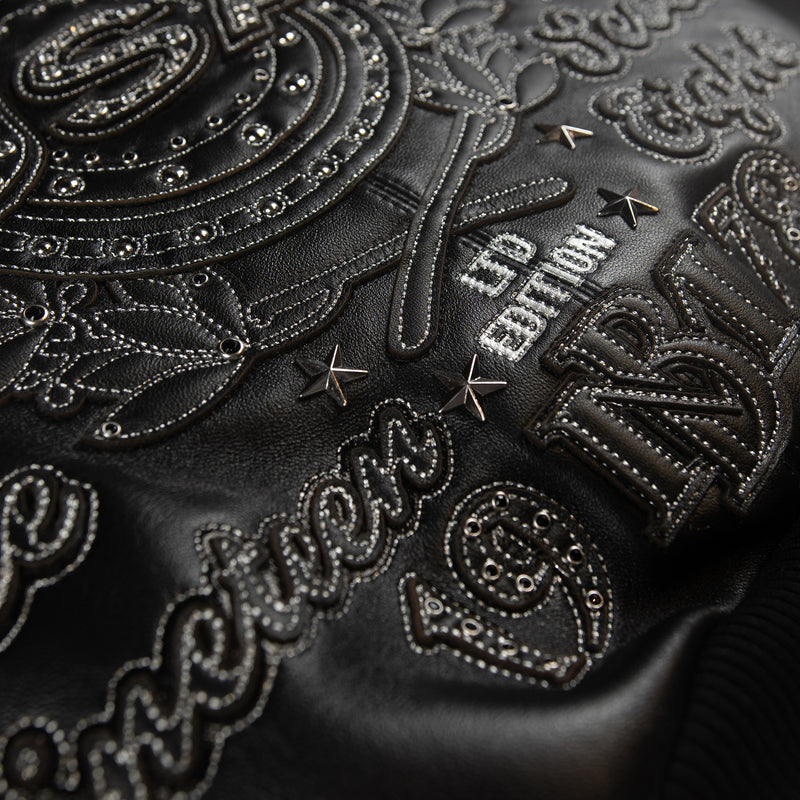 Close-up of black leather racing jacket back showing crest applique, star studs, decorative eyelets and silver-tone embroidered wording.
