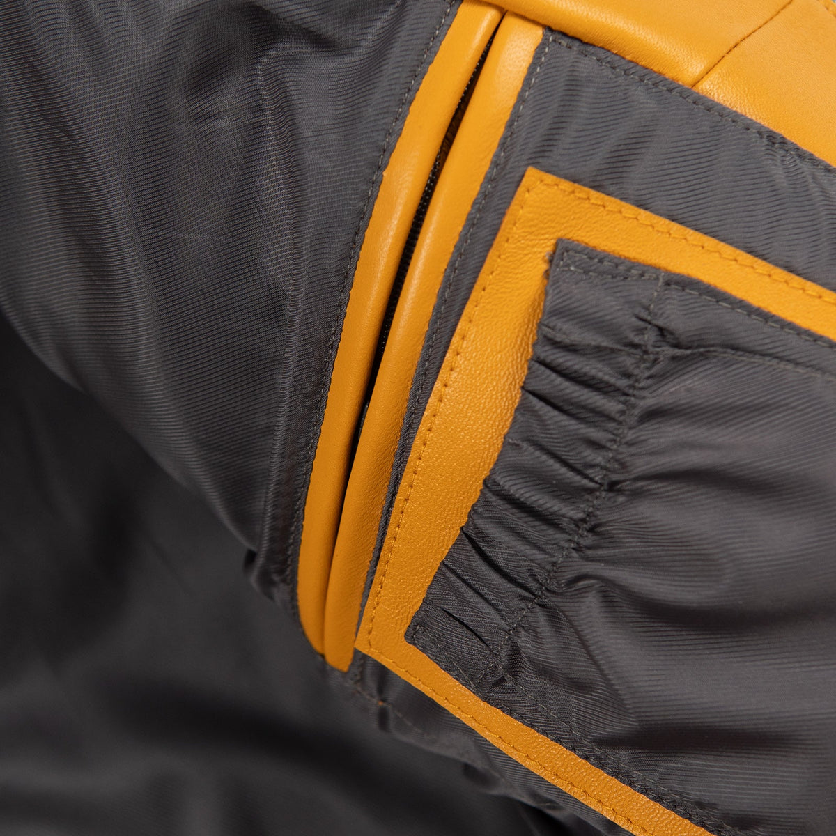 Close-up of dark jacket lining with maize yellow leather pocket trim, stitched edges and a small fabric pocket inside the garment.