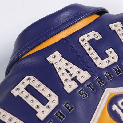Upper back of purple leather varsity jacket showing cream embellished block lettering, stitched panels and contrasting gold collar detail.