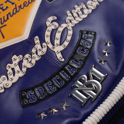 Lower back detail of purple leather jacket with cream script lettering, black applique, silver-tone stars and striped ribbed waistband.