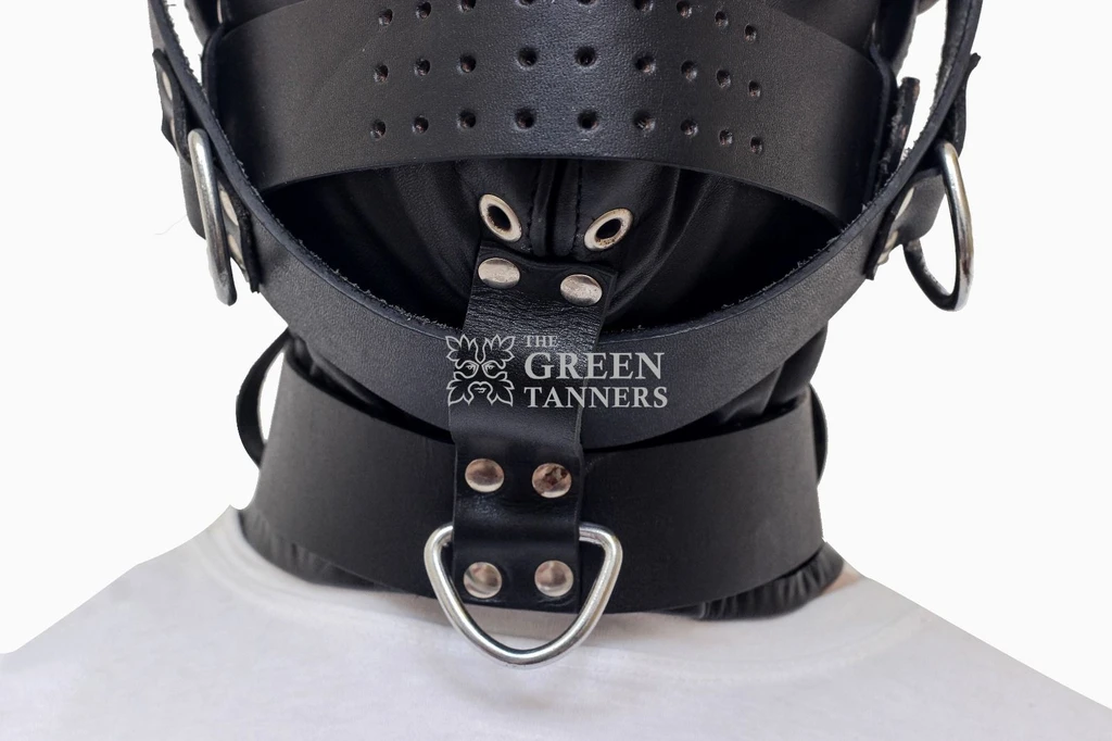 Close-up of a black leather hood showing the perforated face band, metal-rimmed lower openings, broad collar and ringed chin strap detail.