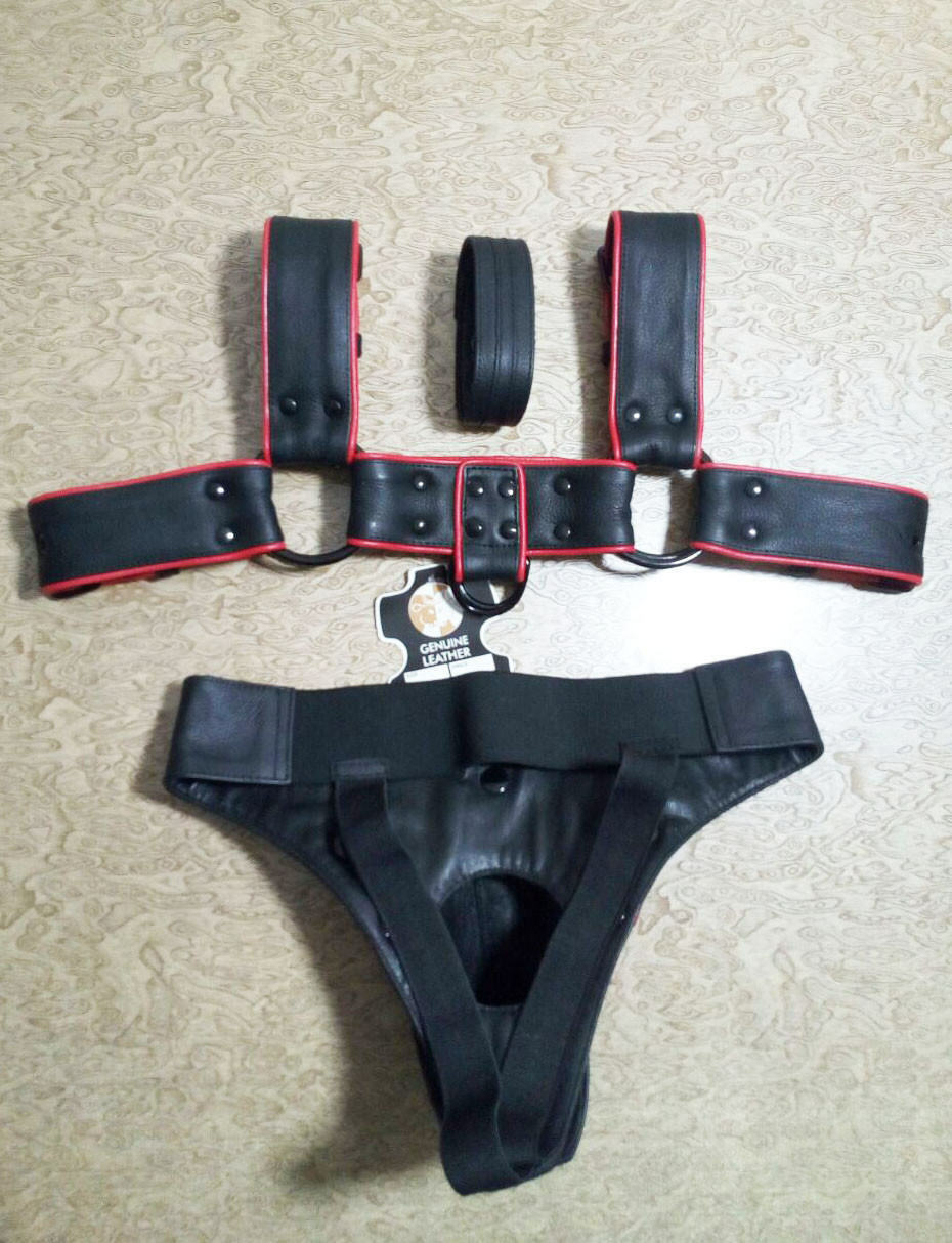 Reverse view of black leather chest harness and matching jockstrap with red trim, riveted strap joins, metal rings and broad rear waistband.