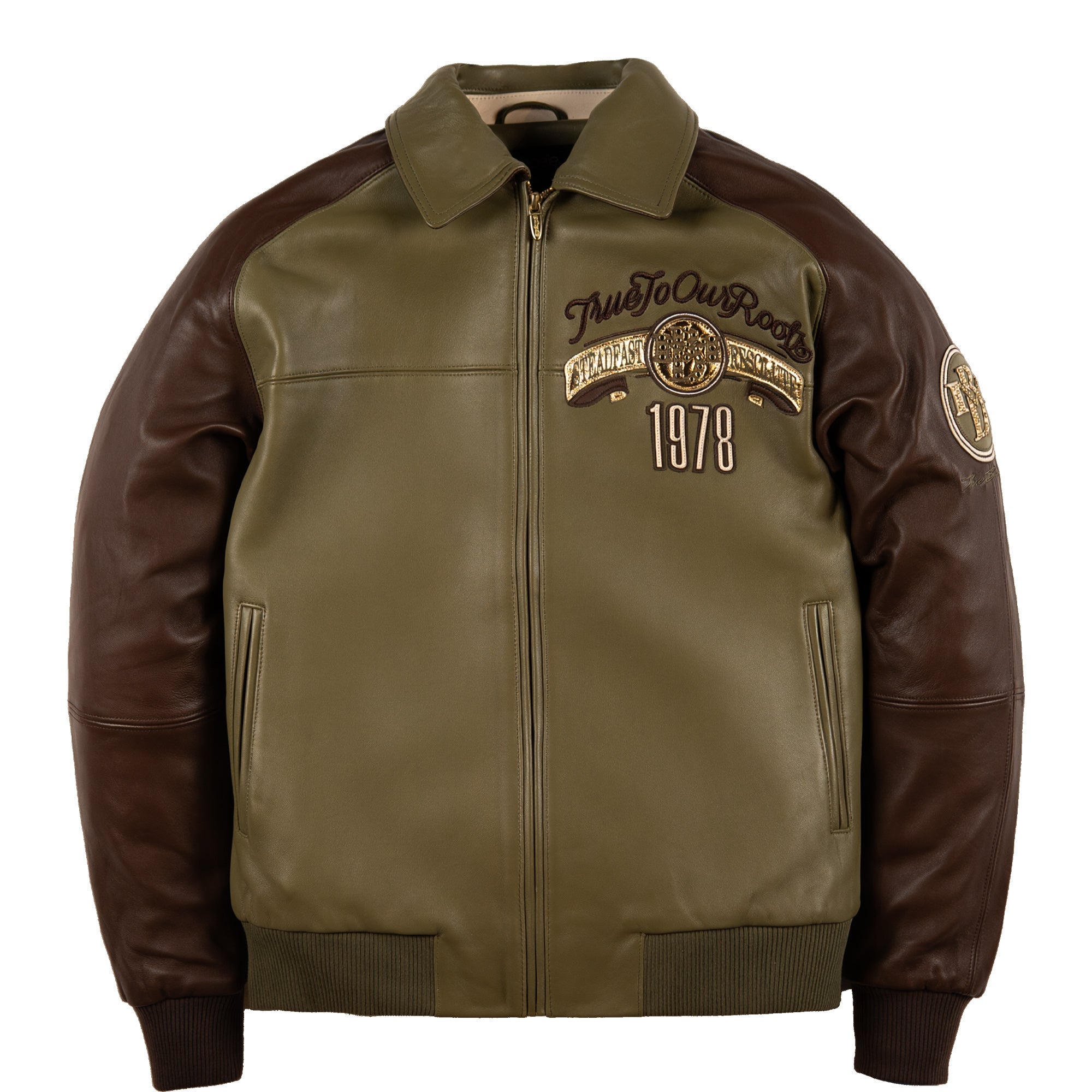An olive green and dark brown leather jacket with a front zipper, ribbed collar, cuffs, and hem. The left chest features a circular patch with the text 'True To Our Roots' and '1978', and there is a circular patch on the right sleeve.