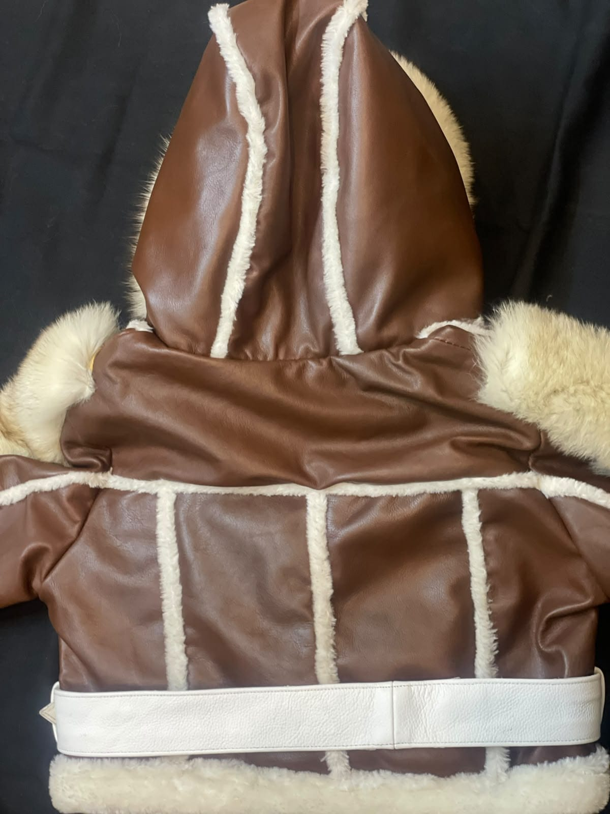 Men's brown hooded leather aviator jacket, rear view showing cream-trimmed panel seams, a large hood, and a white belt across the waist.