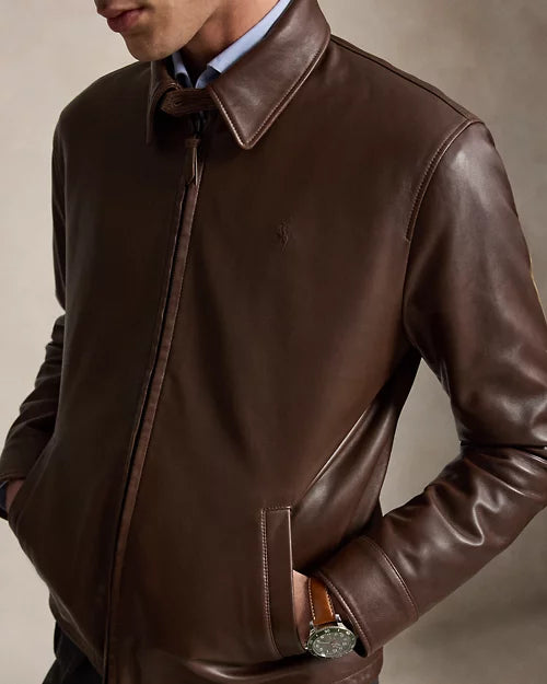 Close-up of a chocolate brown leather jacket showing the pointed collar, front zipper, chest embroidery and narrow lower welt pocket.
