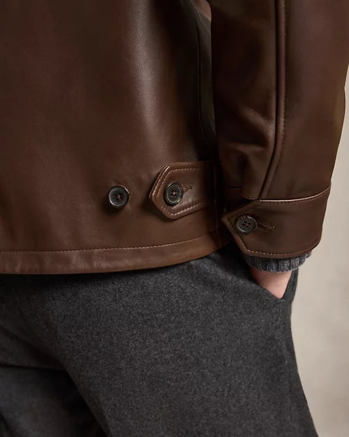 Detail view of a chocolate brown leather jacket showing its buttoned rear waist tab, cuff fastening, stitched edges and smooth leather finish.