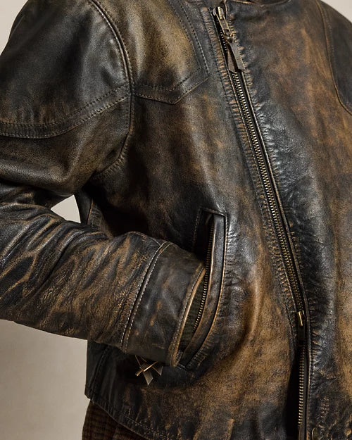 Close-up of a distressed dark brown leather jacket showing the metal front zipper, angled zip pocket, stitched panels and cuff strap detail.