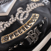 Women's black leather varsity jacket, back applique close-up, showing contrasting cream accents and decorative details in the supplied product photograph.