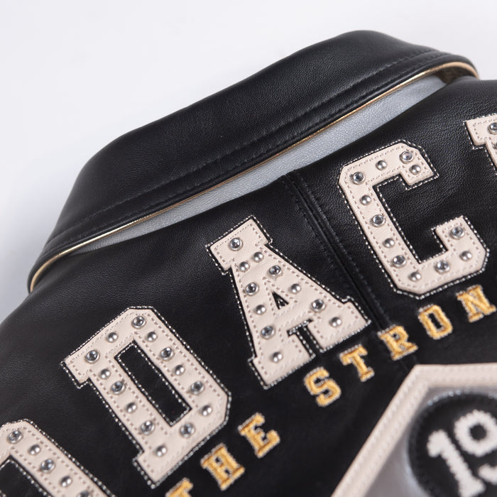 Women's black leather varsity jacket, upper back lettering close-up, showing contrasting cream accents and decorative details in the supplied product photograph.