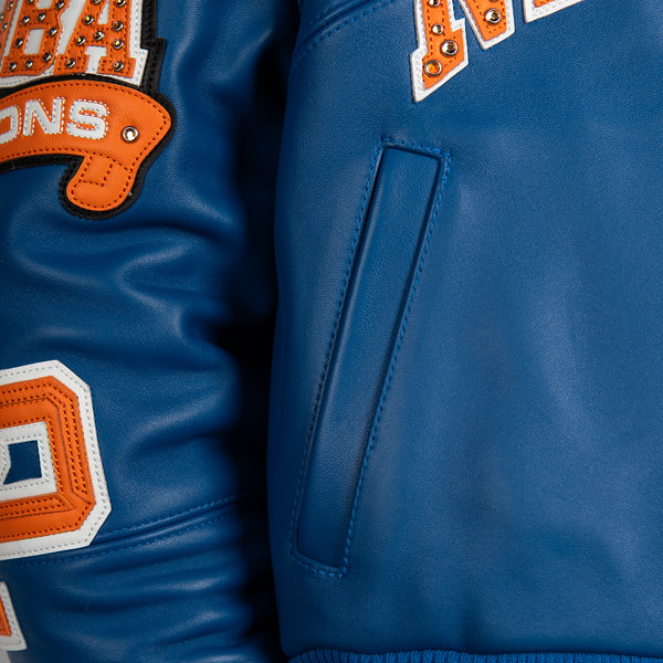 Women's blue and orange leather varsity jacket, front pocket detail, showing New York basketball graphics and contrasting decorative details.