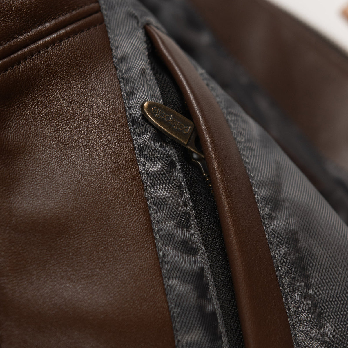 Women's brown colorblock leather racing jacket, interior seam detail, with caramel and olive panels and decorative metallic accents.