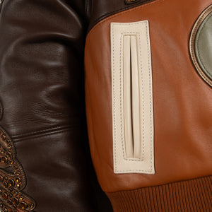 Women's brown colorblock leather racing jacket, contrast zip pocket detail, with caramel and olive panels and decorative metallic accents.