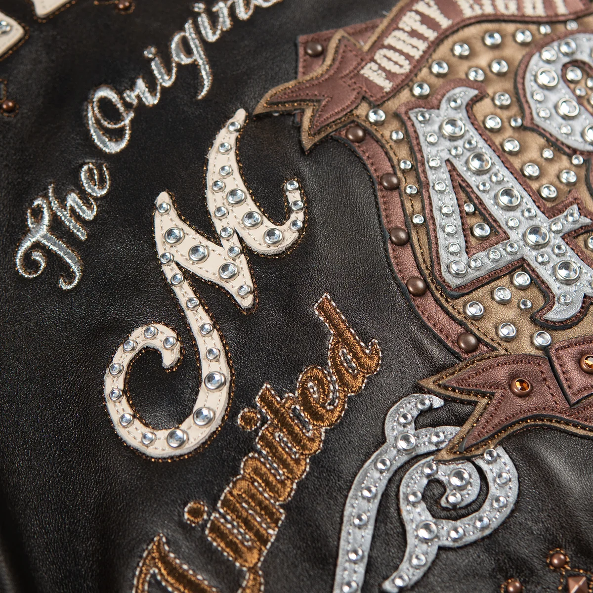 Women's distressed brown leather anniversary jacket, back crest close-up, with cream lettering, layered crest artwork, and reflective embellishments.
