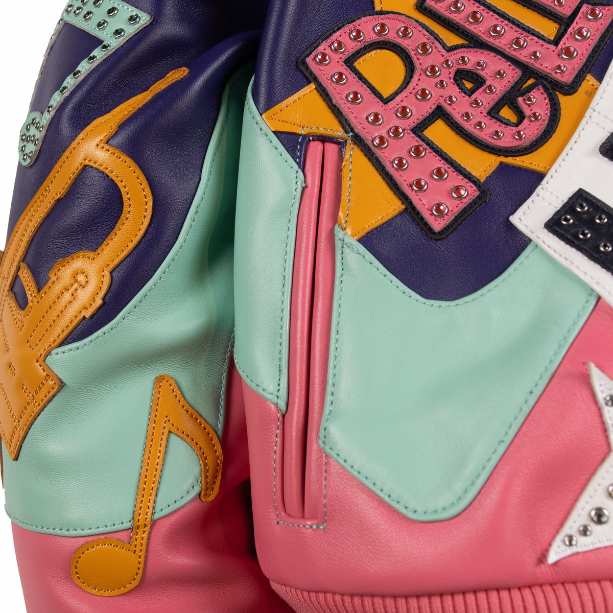Pocket detail of a multicolor leather music jacket showing a pink welt opening, mint panel, purple leather and yellow musical note appliques.