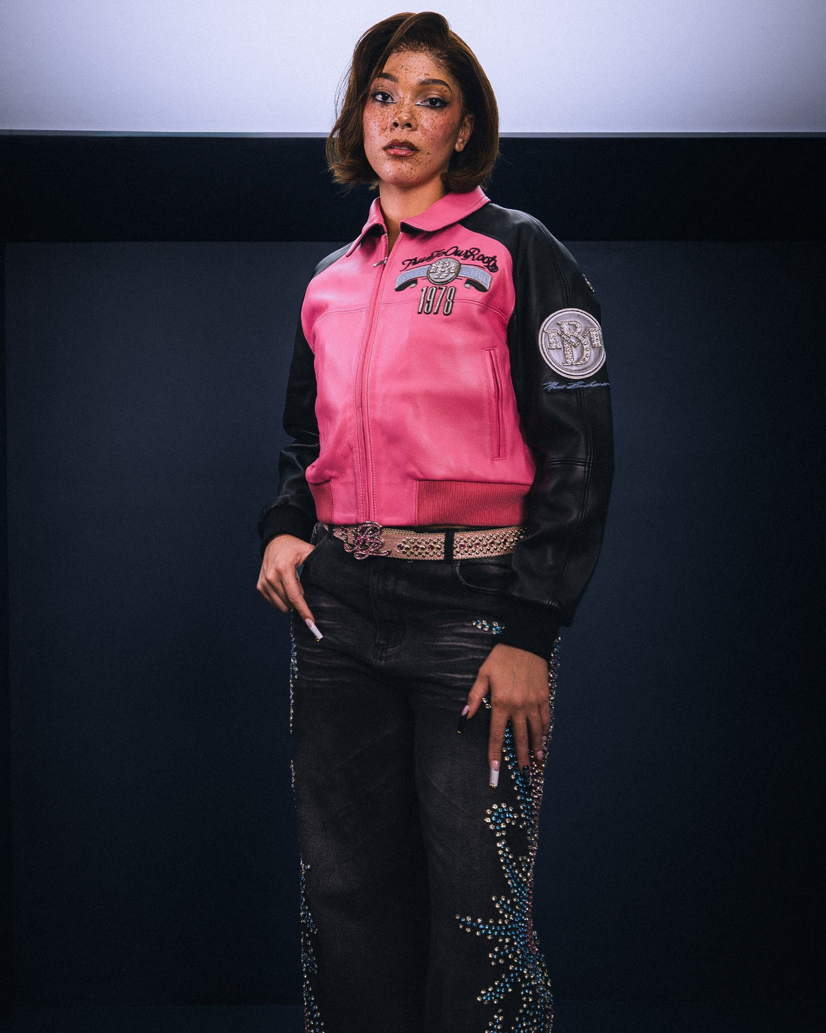 Women's pink and black leather varsity jacket, styled model view, featuring contrast panels and decorative lettering in the product photo.