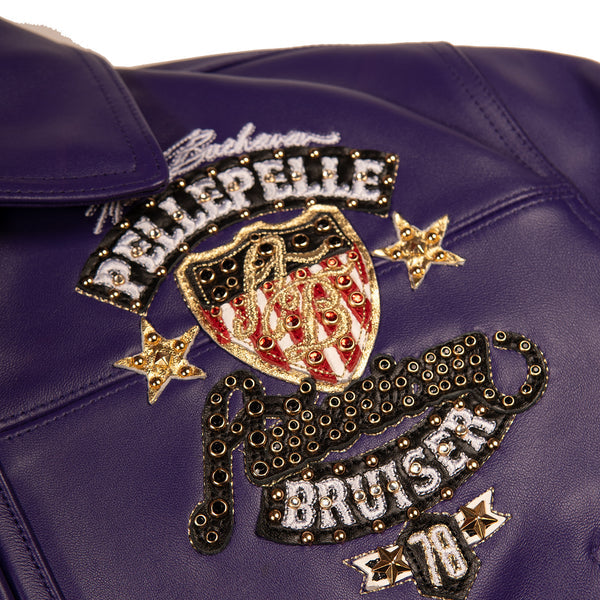 Women's purple leather bomber jacket, chest crest close-up, with gold-toned embellishments, cream accents, and decorative crest artwork.