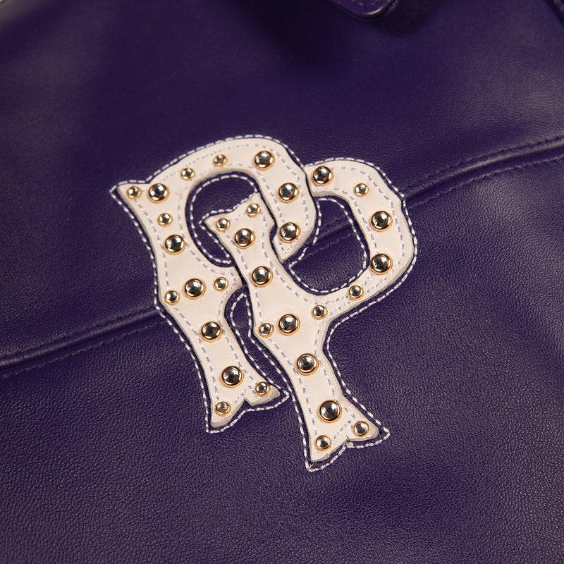Women's purple leather bomber jacket, studded monogram detail, with gold-toned embellishments, cream accents, and decorative crest artwork.