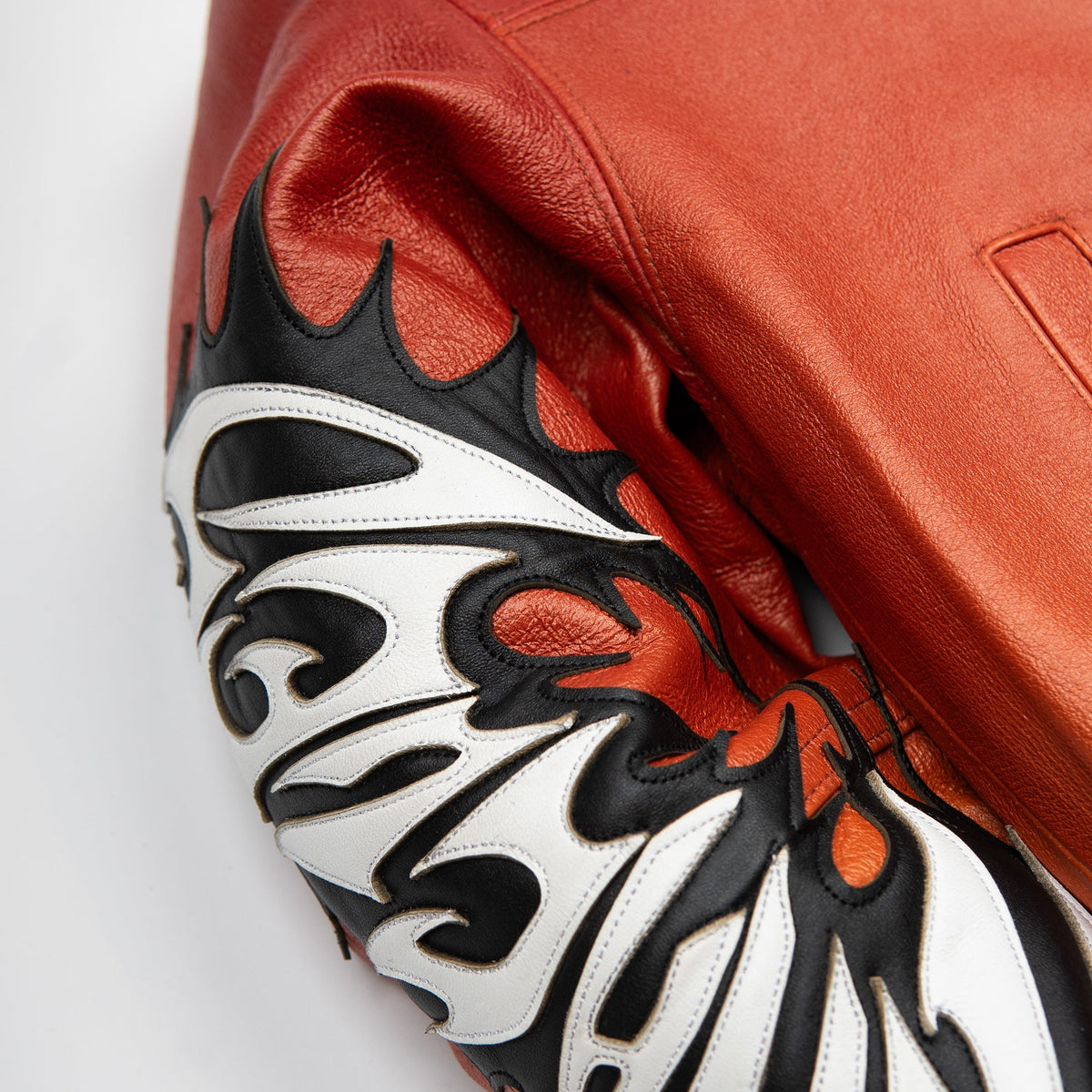 Women's red orange gradient leather bomber jacket, sleeve applique close-up, showing contrasting black and white graphics and warm-toned panels.