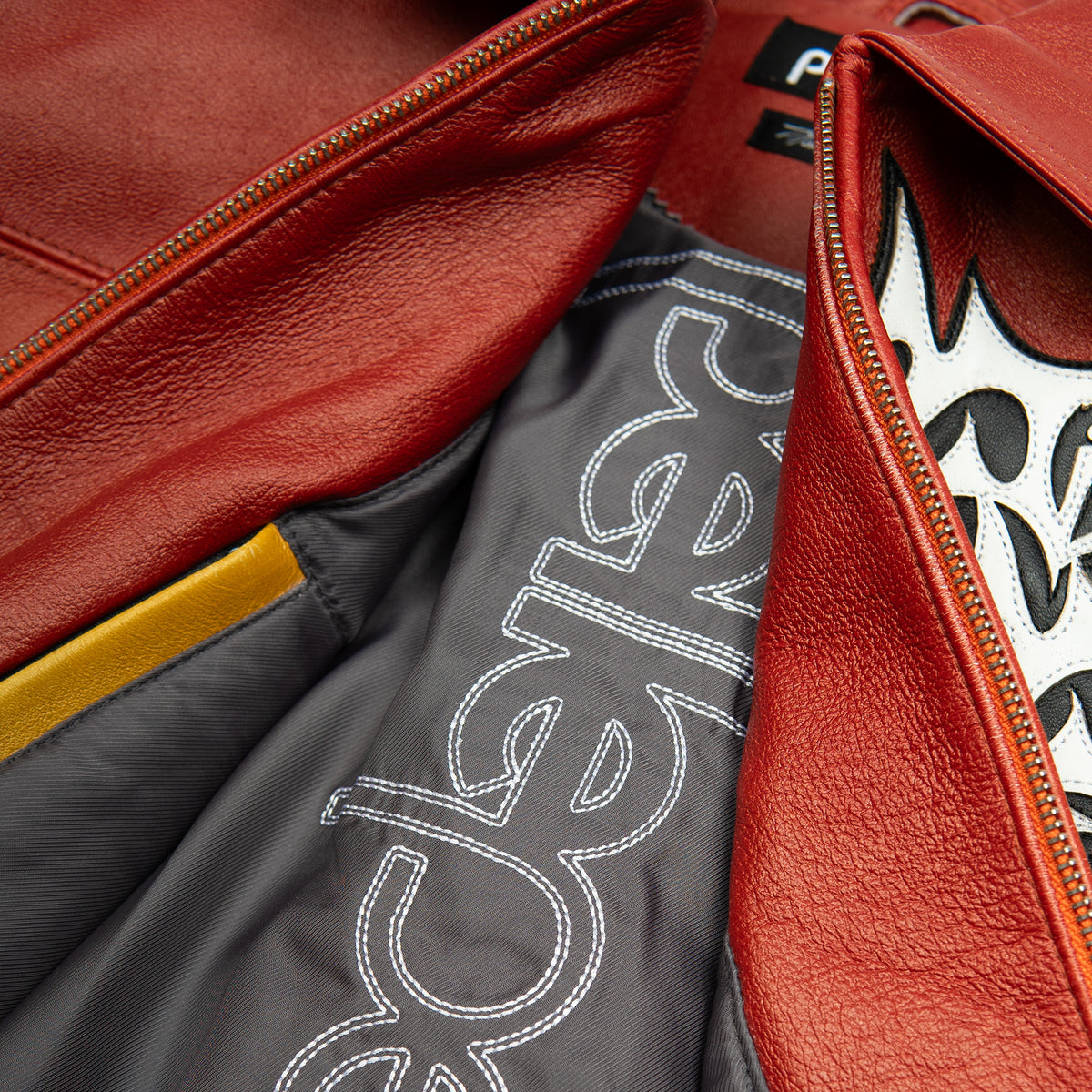 Women's red orange gradient leather bomber jacket, interior lining close-up, showing contrasting black and white graphics and warm-toned panels.