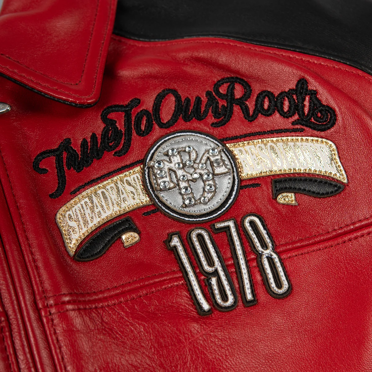 Women's red and black leather varsity jacket, chest emblem close-up, with contrasting panels, embroidered motifs, and reflective embellishments.