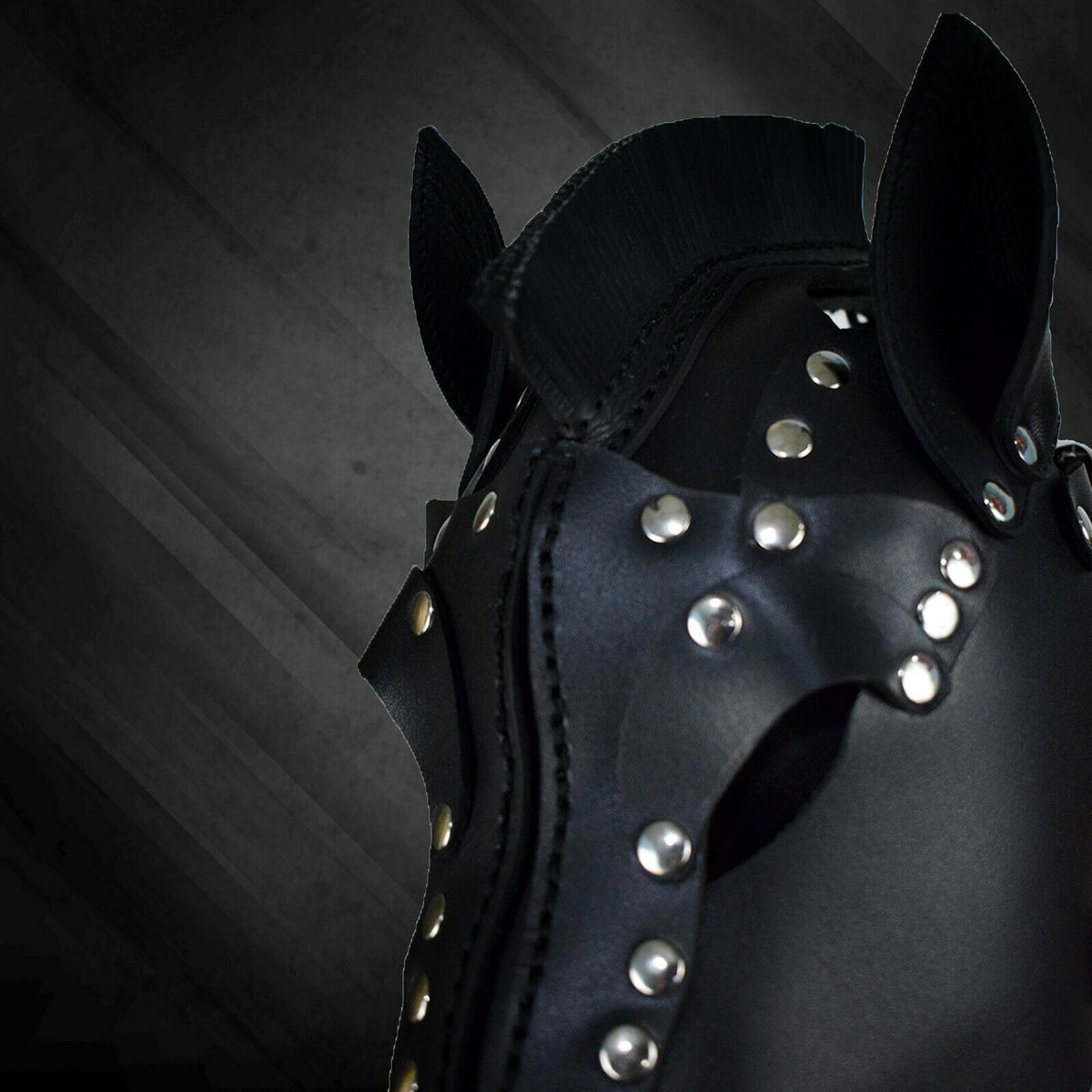 Close-up of black leather horse mask showing the stitched center seam, layered eye panels, pointed ears and silver-tone stud details.