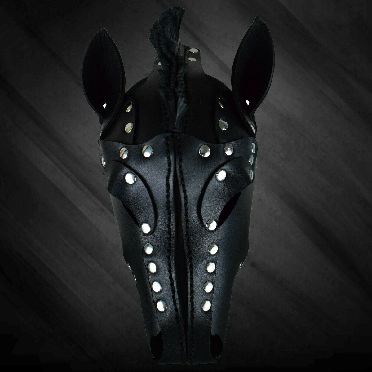Upper front view of black leather horse mask with upright ears, narrow fringe mane, studded eye surrounds and a stitched central seam.