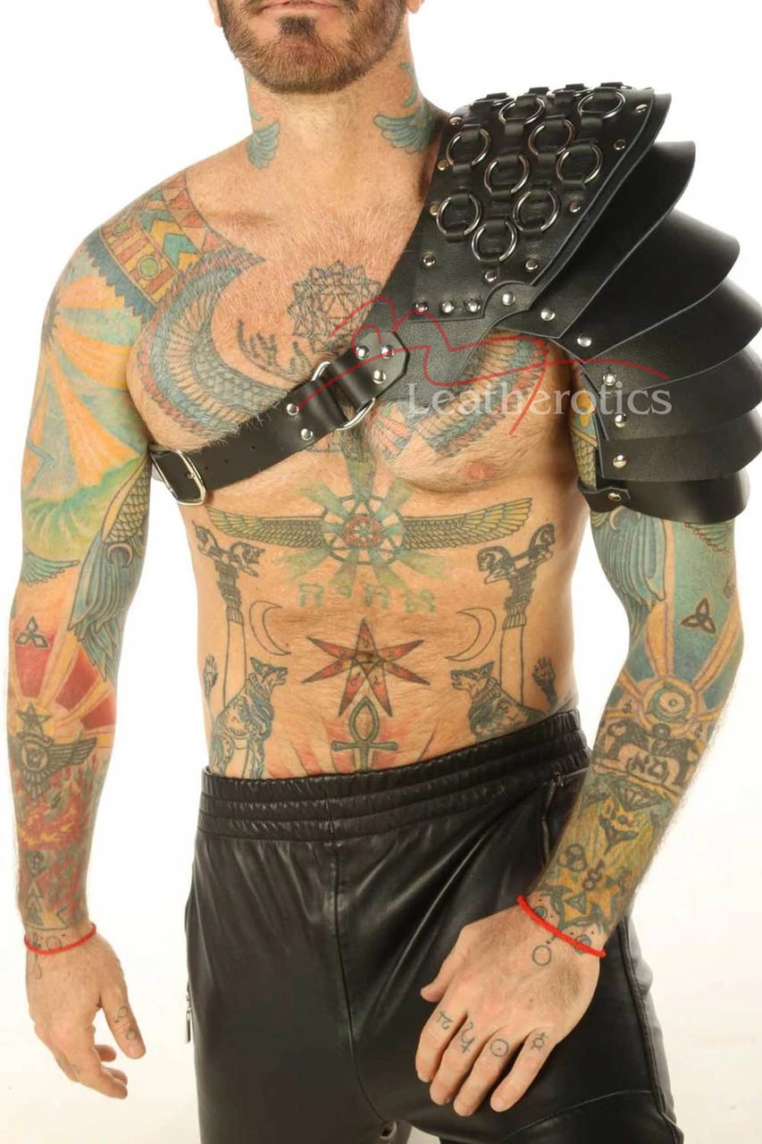Black leather layered shoulder armor harness, front view with overlapping shoulder panels, decorative metal rings and a diagonal buckle strap.