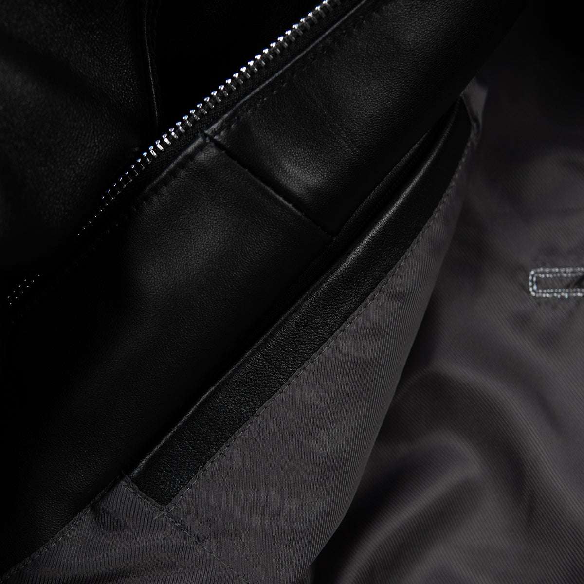 Interior detail of black leather jacket showing zipper teeth, smooth leather facing and dark lining beside a stitched panel seam.