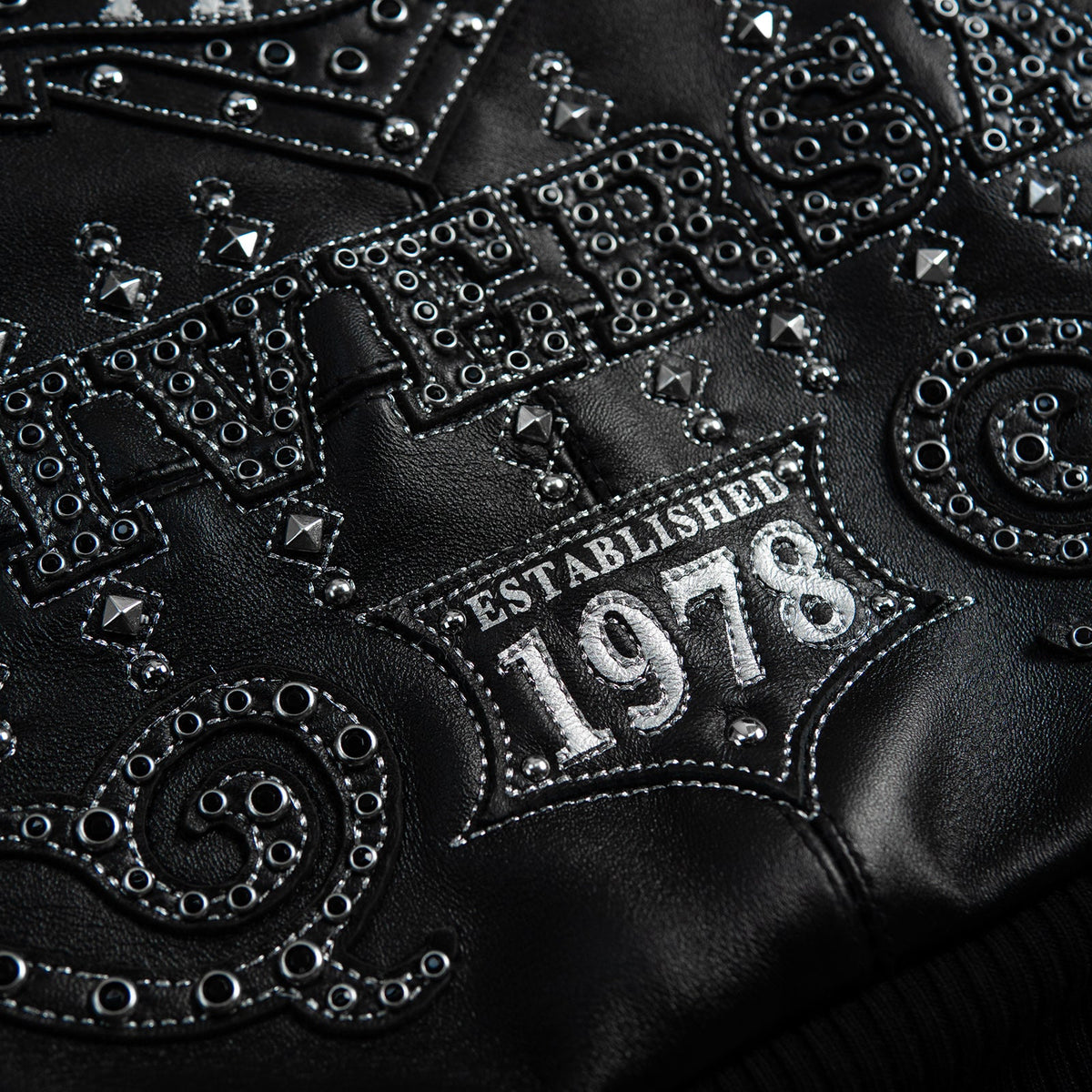 Lower back detail of black leather jacket with embellished anniversary lettering, scroll applique, silver-tone studs and 1978 patch.