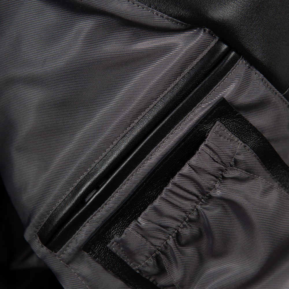 Interior pocket detail of black leather jacket showing dark fabric lining, leather-trimmed opening and gathered fabric pocket panel.