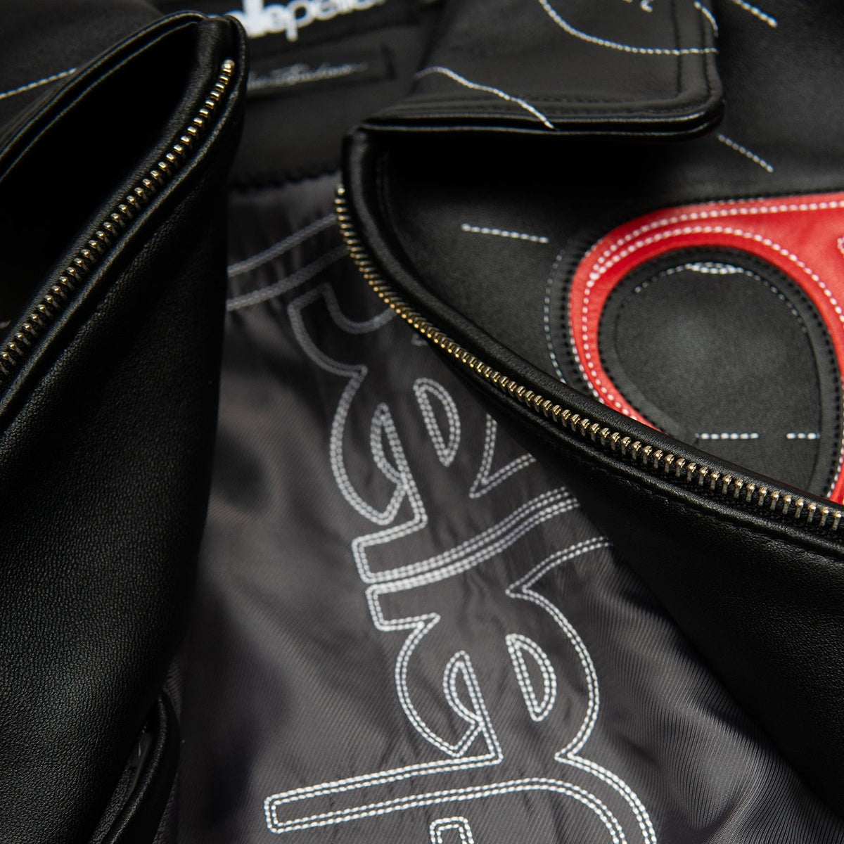 Women's black leather contour stitch bomber jacket, interior view showing dark fabric lining, stitched lettering and the front zipper.